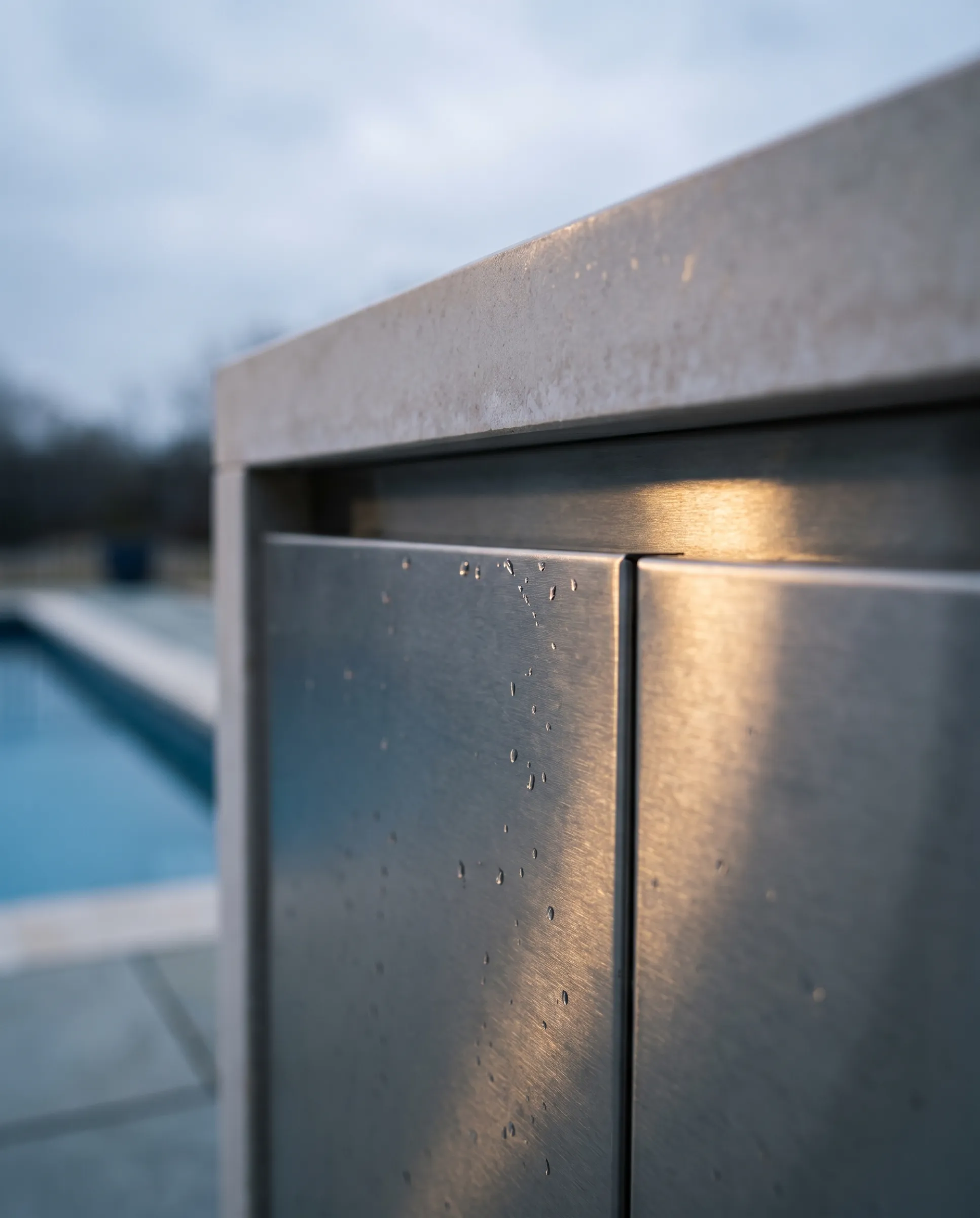 Close detail of brushed marine-grade stainless cabinet fronts with a shadow gap reveal and honed limestone counter
